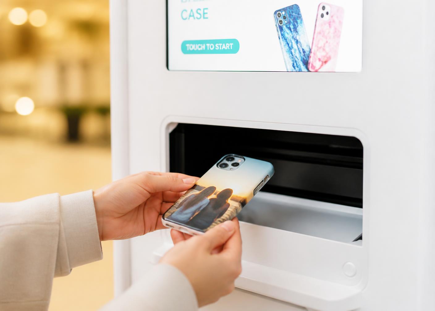 Manos recogiendo una funda personalizada recién impresa de la bandeja del kiosco